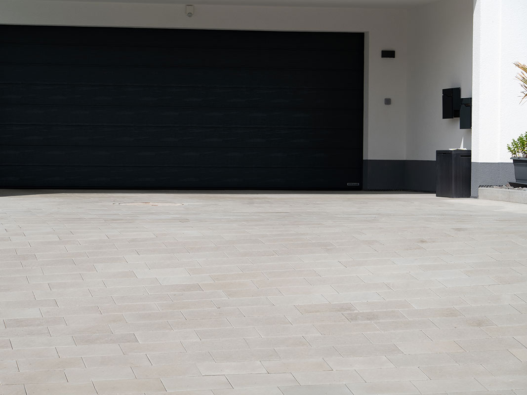 Schwarze Garage der Familie Grimm mit gepflasterter Hofeinfahrt und modernem Gartendesign