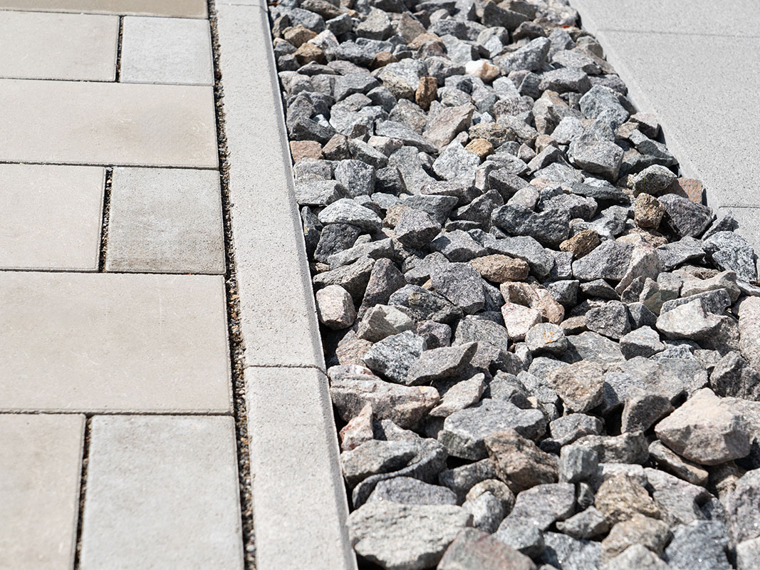 Übergang von gepflastertem Bereich zu Steinrand mit locker verlegten Steinen in der Gartenanlage Familie Grimm