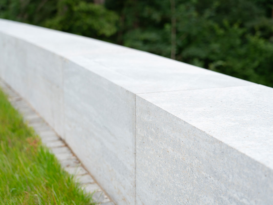 Niedrige Mauer aus Beton in der Außenanlage der Nussbaum GmbH, umgeben von naturnah gestalteten Wegen