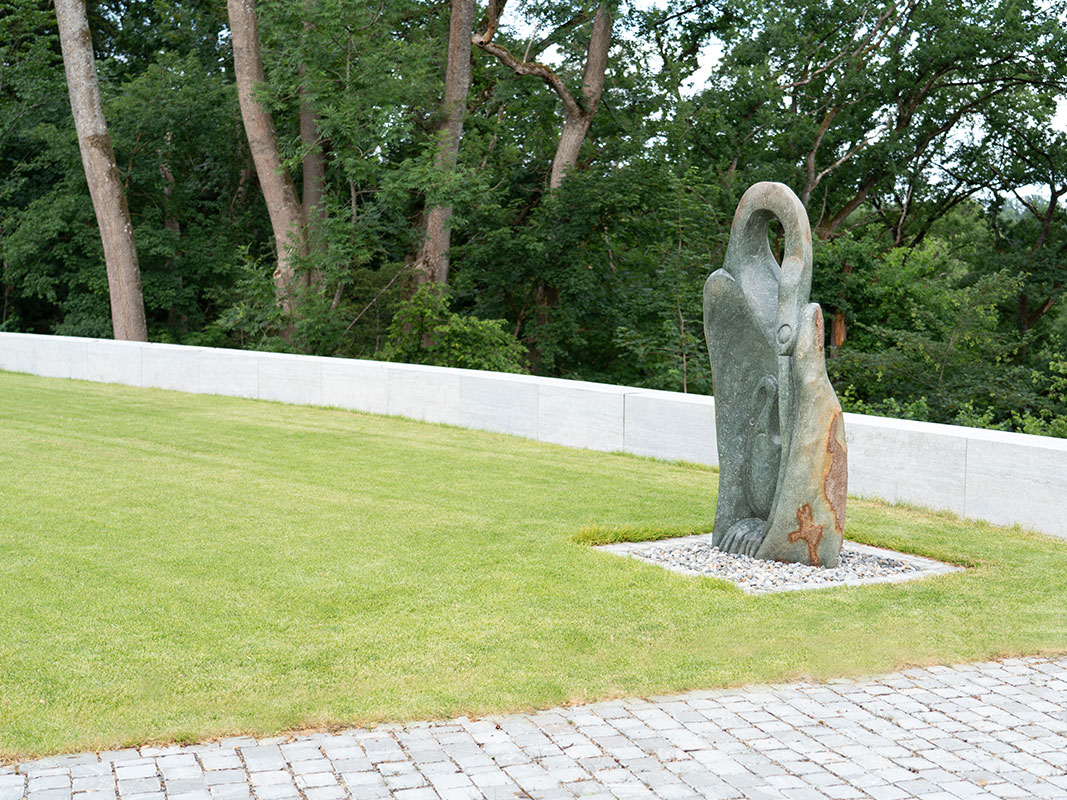 Grüne Rasenfläche mit einer modernen Skulptur, abgegrenzt durch eine niedrige Betonmauer, Teil der Außenanlage der Nussbaum GmbH in Rottweil.