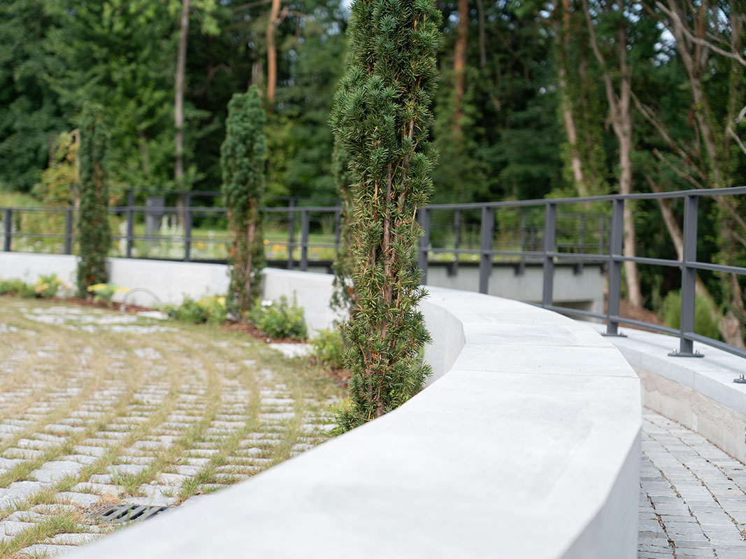 Kleine, im Bogen angeordnete Betonmauer mit Metallgitter dahinter.