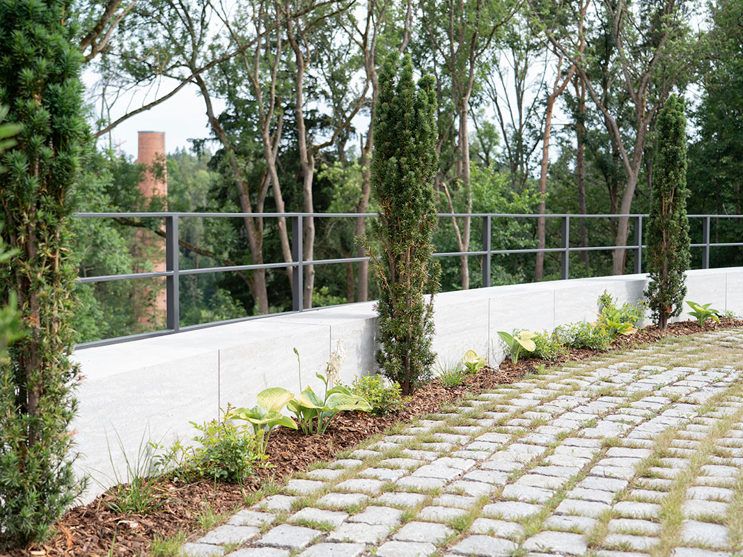 Kleine, im Bogen angeordnete Betonmauer mit Metallgitter dahinter.