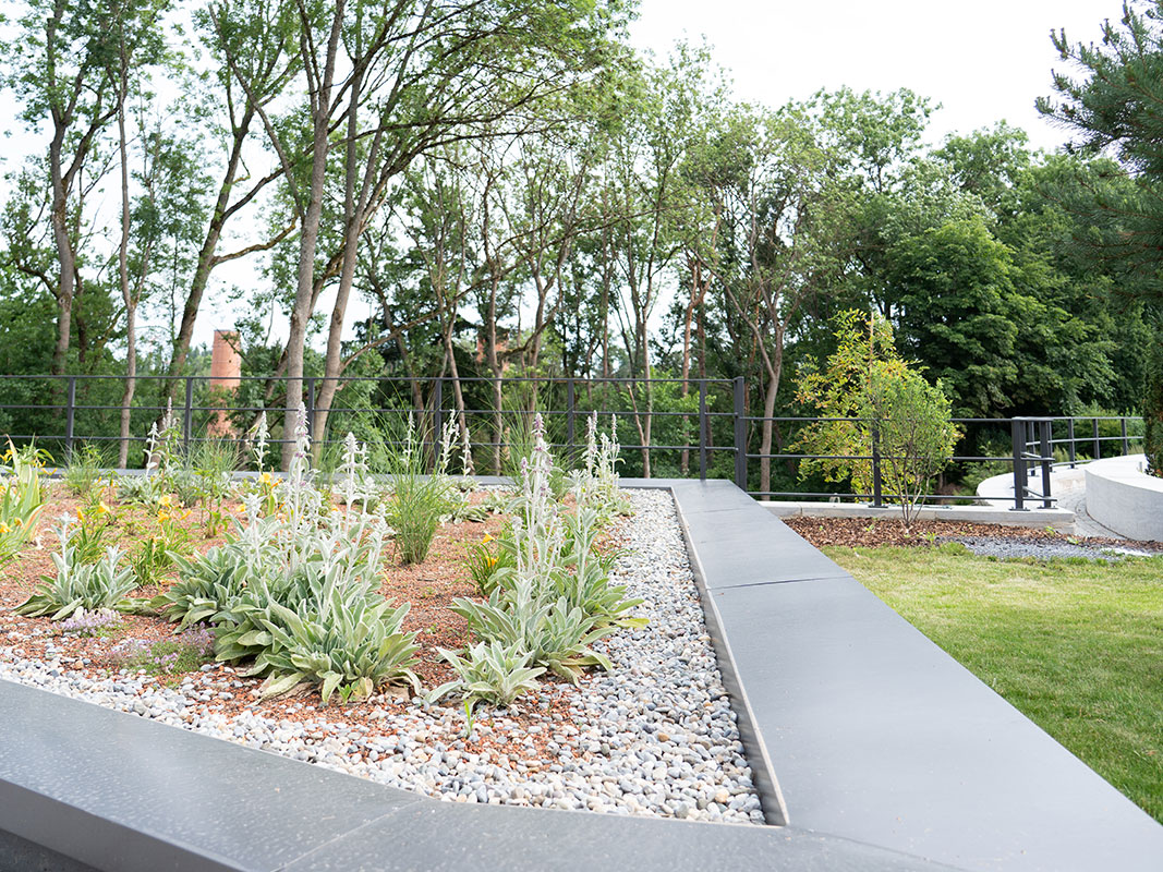 Erhöht angelegtes Gräserbeet in Dreiecksform mit Metallrahmen und Kieselstein-Einfassung