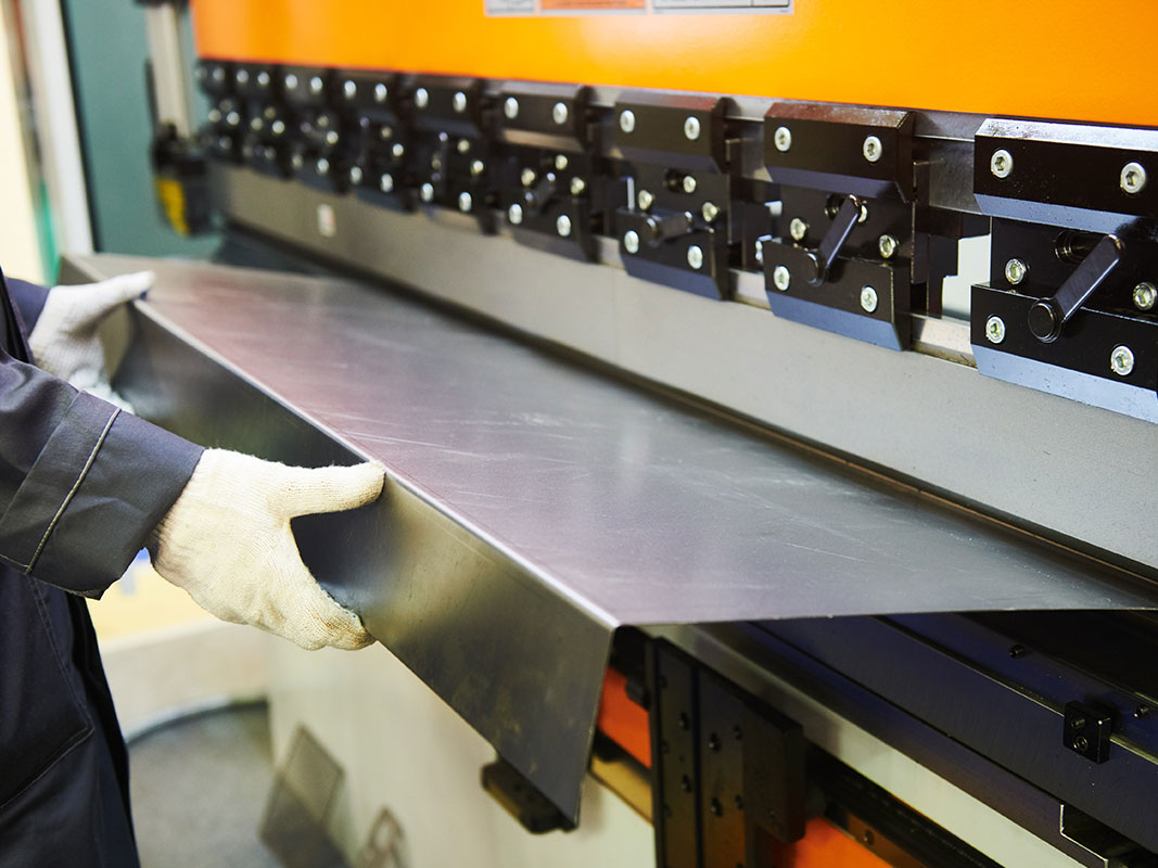 Mann mit weißen Handschuhen hält ein frisch ausgestoßenes Blech aus einer Blechmaschine.