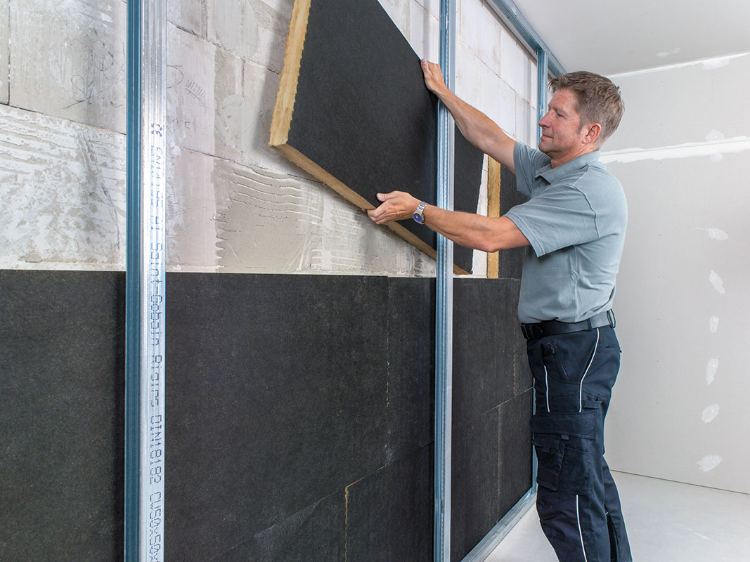 Ein Mann installiert Hartschaumplatten als Dämmung an einer Mauer beim Bau oder Sanierung.