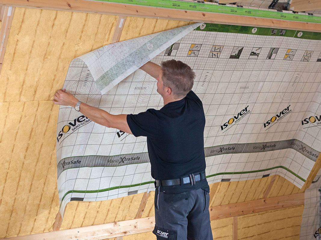 Mann bringt Dämmmaterial an einer Dachschräge an und zieht die Schutzfolie von der Platte ab.