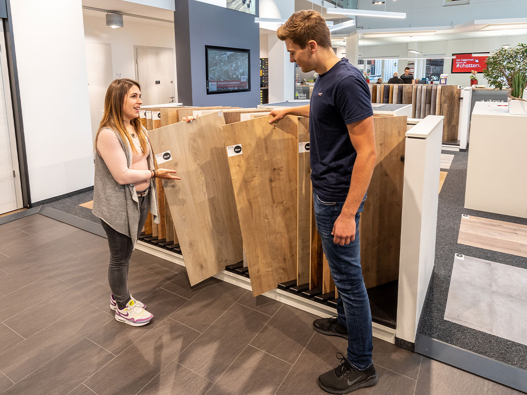 Verkäuferin zeigt einer Kundin im Ausstellungsraum eine Holzbodenbelagplatte