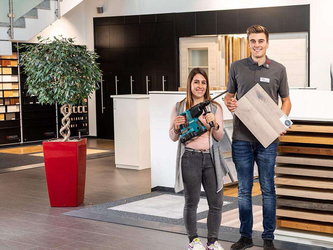 Zwei Auszubildende im Ausstellungsraum von Jäckle+Flaig: Sie hält eine Bohrmaschine, er eine Holzplatte