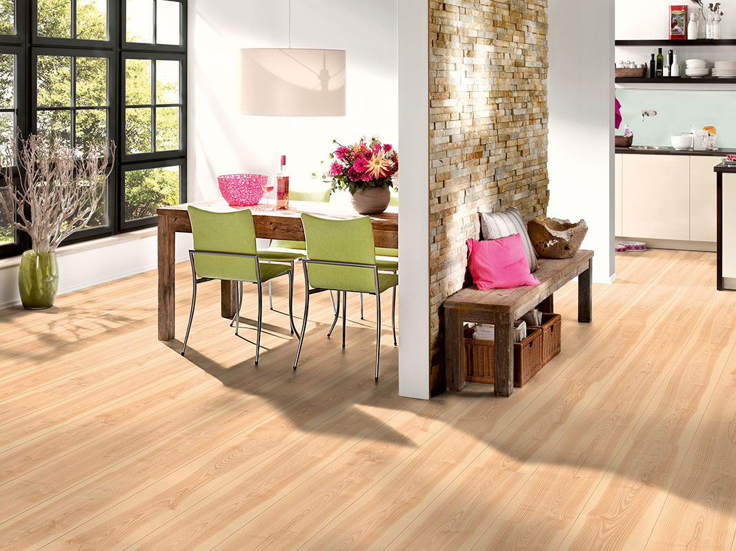 Essbereich mit vier hellgrünen Stühlen an einem Tisch, der an einer Wand steht, auf hellem Laminatboden.