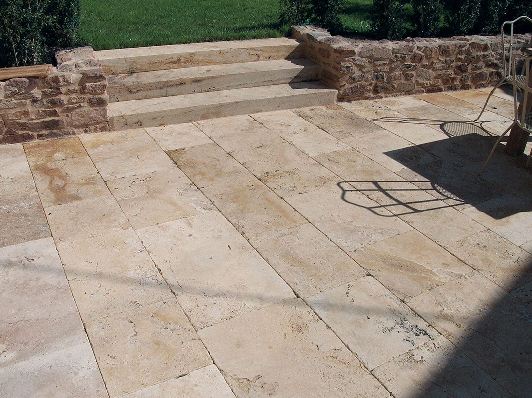 Terrasse aus Natursteinplatten mit kleinem Treppenaufgang zum Rasen und einer kleinen gemauerten Begrenzung.