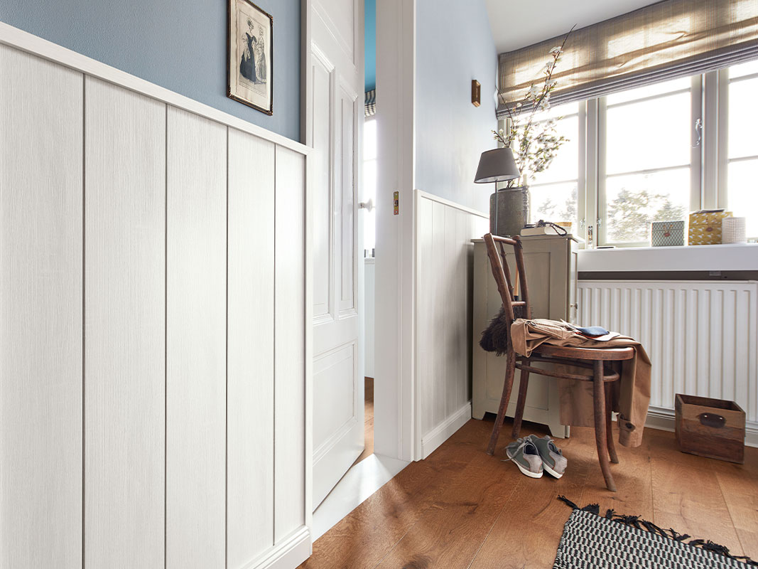 Innenraum mit halbhoher Holztäfelung an der Wand, Holztür auf der linken Seite und einem Holzstuhl in der Ecke – Beispiel für dekorative Wandgestaltung mit Paneelen.