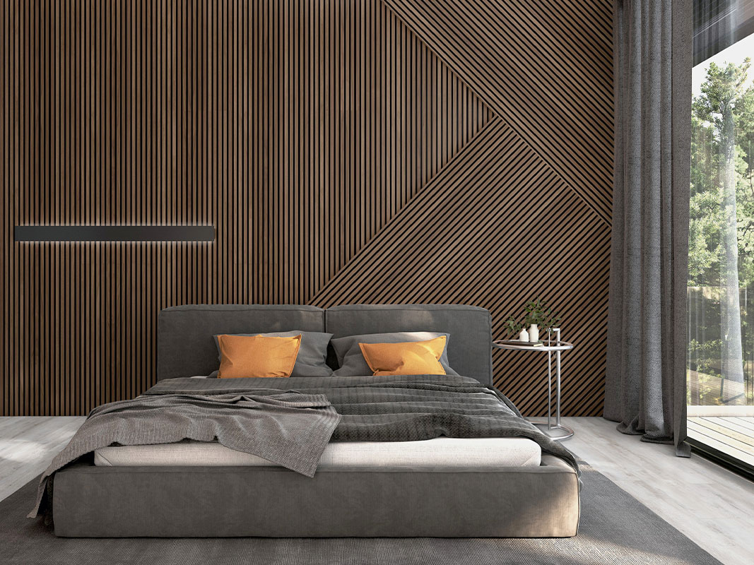 Moderne Schlafzimmerwand aus Akustikpaneelen mit integrierter Beleuchtung, davor ein graues Doppelbett mit orangefarbenen Kissen.