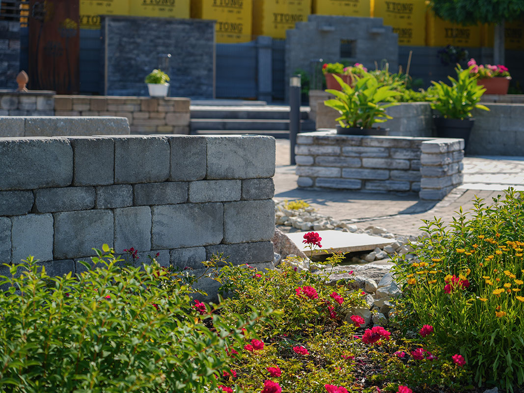 Steingartenausstellung in Niedereschach mit Pflastersteinen, Steinmauern, grünen Pflanzen und Rosen im Vordergrund.