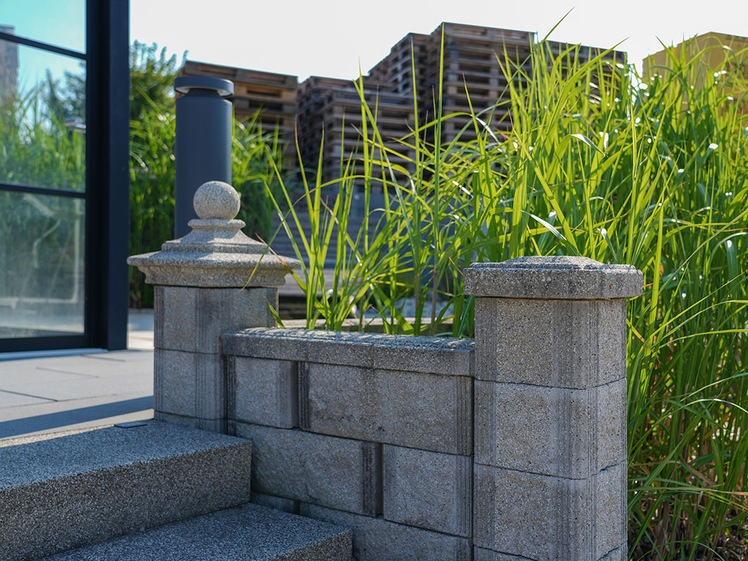 Steingartenausstellung mit Mauer neben Treppe, kleinem Turm und hohen Gräsern im Hintergrund