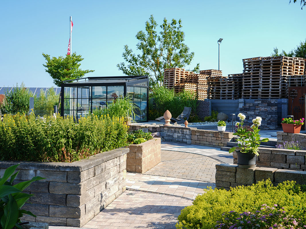 Steingartenausstellung in Niedereschach mit gebogenem Weg aus verschiedenen Pflastersteinen und erhöhten Blumenbeeten, abgegrenzt durch Steinmauern