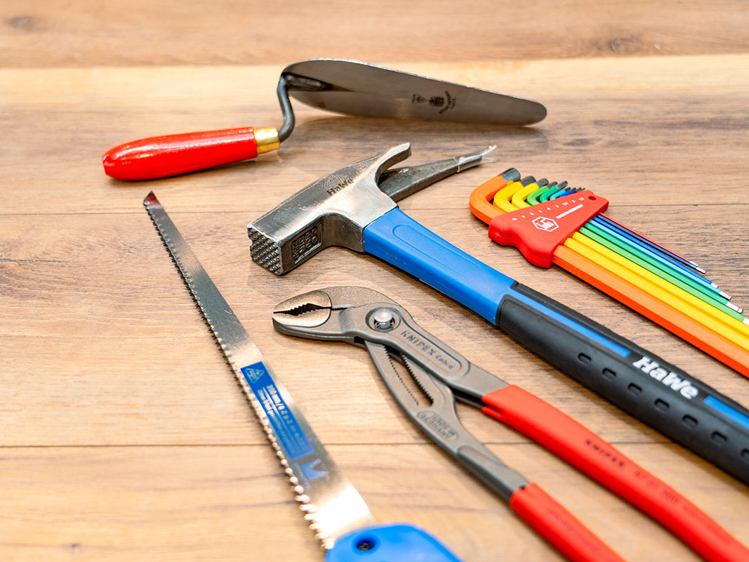 Handwerkzeuge wie Spachtel, Zange, Säge, Hammer und verschiedene Werkzeugaufsätze.