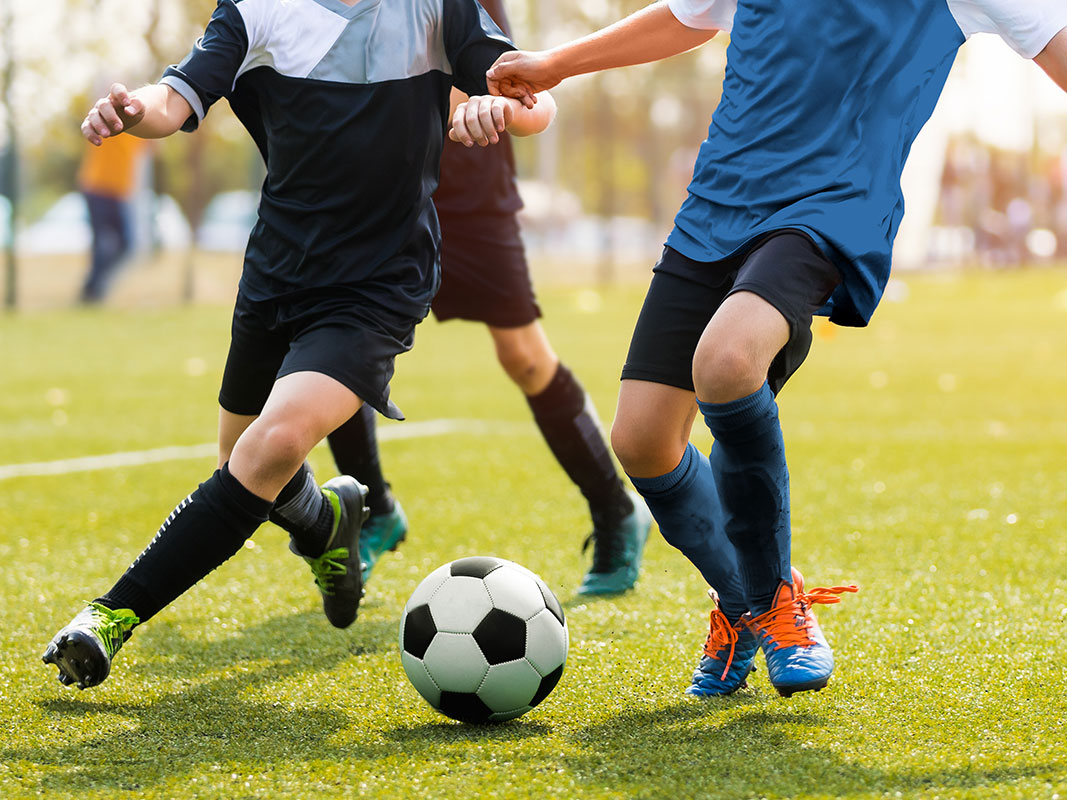 Beine von spielenden Kindern beim Fußballspielen auf einer Wiese.