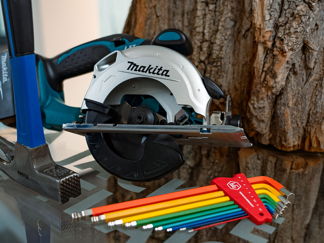 Werkzeugsatz in bunten Farben, Kreissäge von Makita und Hammer, im Hintergrund ein Baum.