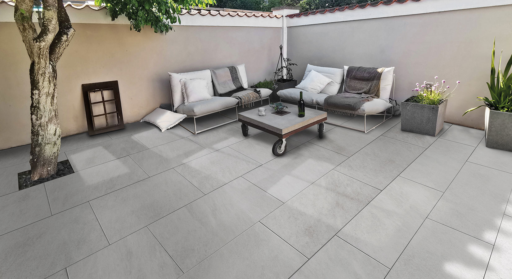 Terrasse aus großen Steinplatten, umrahmt von einer Mauer, mit zwei Blumenkübeln und Sitzgelegenheiten mit Tisch