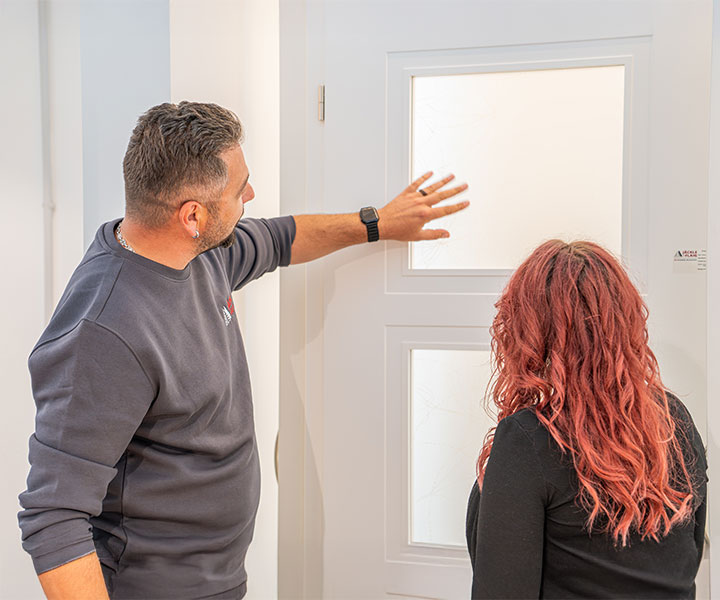 Berater erklärt Kundin Glaseinsätze einer weißen Tür im Ausstellungraum