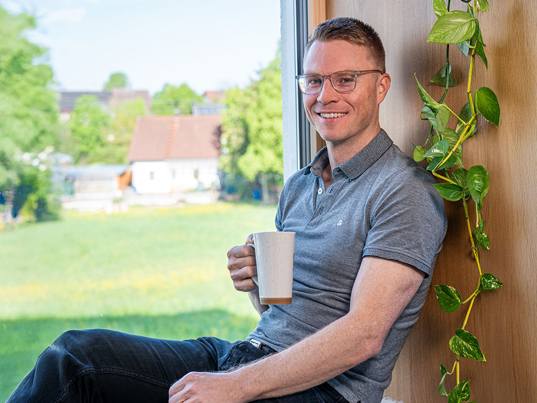 Hausherr sitzt entspannt mit Kaffeebecher in einer Holzfensternische.