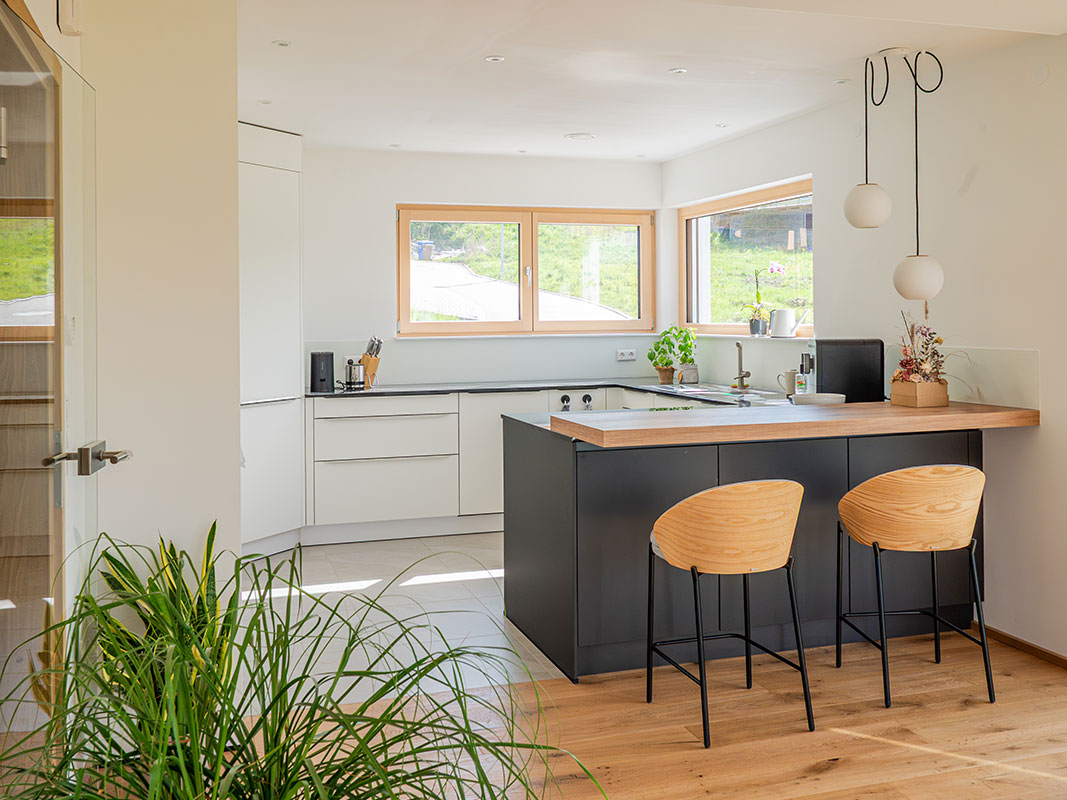 Offene weiße Küche mit kleiner Bar und zwei Barhockern.