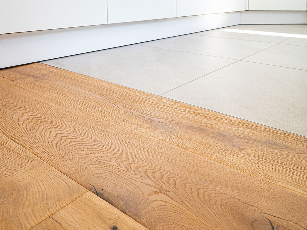 Übergang zwischen weißen Küchenfliesen und Echtholz-Parkettboden in Großaufnahme.